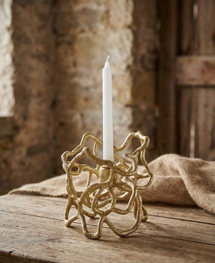 Gold candle holder with a white candle on a wooden surface with a stone wall background